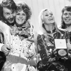 Zespół ABBA świętuje zwycięstwo na Eurowizji. Członkowie zespołu, w błyszczących strojach, radośnie pozują do zdjęcia z nagrodą.