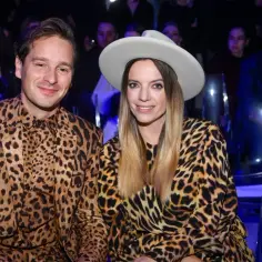 Krzysztof Zalewski i jego żona w identycznych, panterkowych stylizacjach. Uśmiechnięci siedzą obok siebie, ona w kapeluszu.