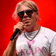 Skolim w okularach i białej koszulce z napisem "SKOLIM" śpiewa na czerwonym tle. Ciekawe, ile Skolim bierze za koncert.