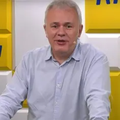 Mazurek z RMF FM w jasnej koszuli, na tle żółto-białej ściany z logo stacji.