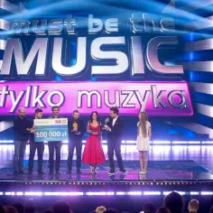 Zwycięzcy "Must be the music. Tylko muzyka" odbierają nagrodę 100 000 zł na scenie, oświetlonej niebieskimi światłami.