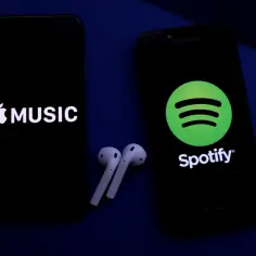 Dwa smartfony z logotypami Apple Music i Spotify, obok słuchawki bezprzewodowe.