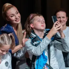 Cleo z dziećmi na scenie. Dziewczynki z kucykami i chłopiec robiący zdjęcie telefonem.