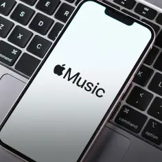 Telefon z logo Apple Music leży na klawiaturze laptopa. Sprawdź aktualną apple music cena.
