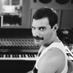 Freddie Mercury w studiu, obok pianina. Wyobraź sobie, że to jego **dzieci** słuchają jego muzyki.