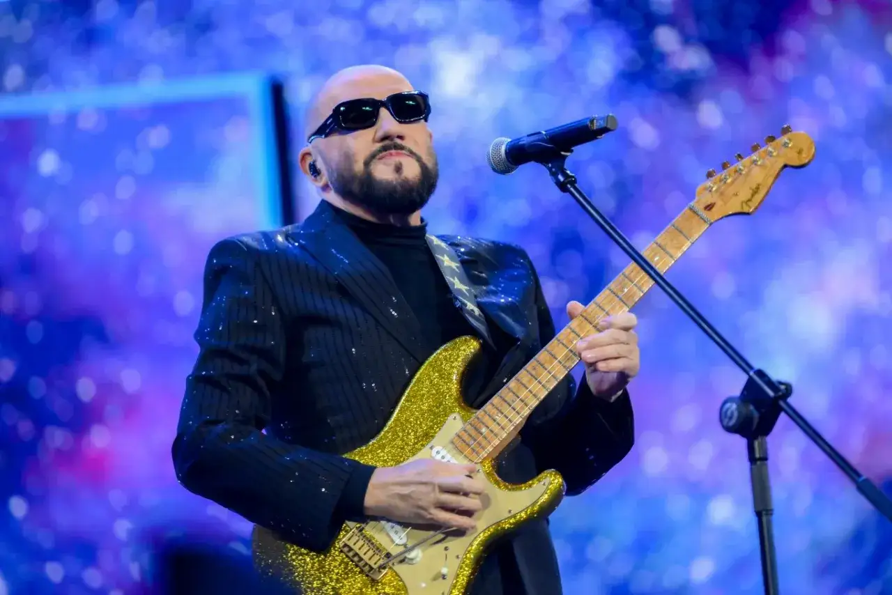 Polscy piosenkarze na scenie. Artysta w błyszczącym garniturze gra na złotej gitarze elektrycznej, w okularach przeciwsłonecznych.