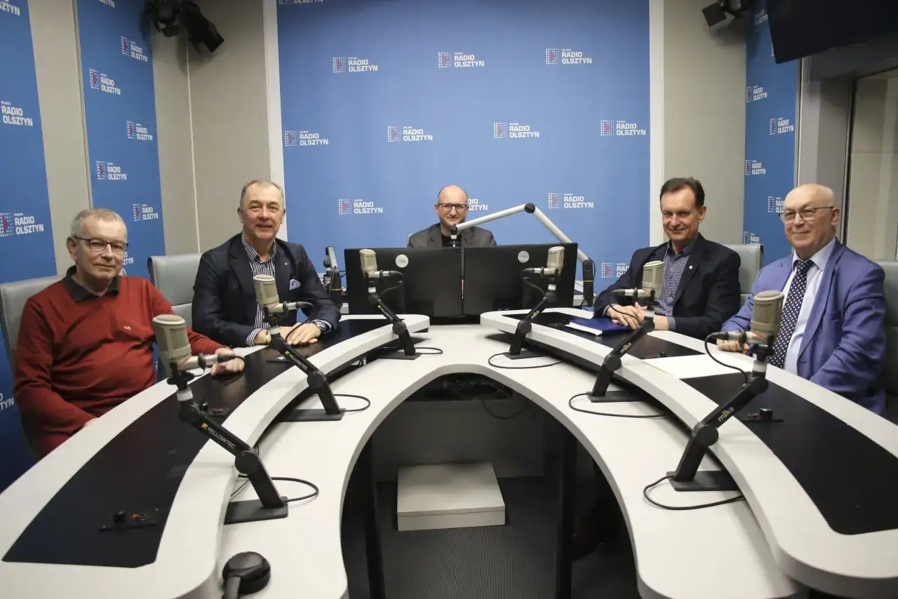 Pięciu mężczyzn siedzi przy stole w studiu radiowym, przygotowując się do nagrania. Ich ramówka jest gotowa.