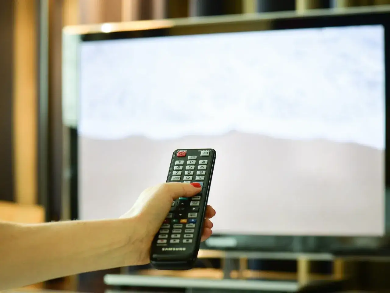 Dłoń z czerwoną hybrydą trzyma pilot od telewizora. Zastanawiasz się, kto nie musi płacić abonamentu RTV?