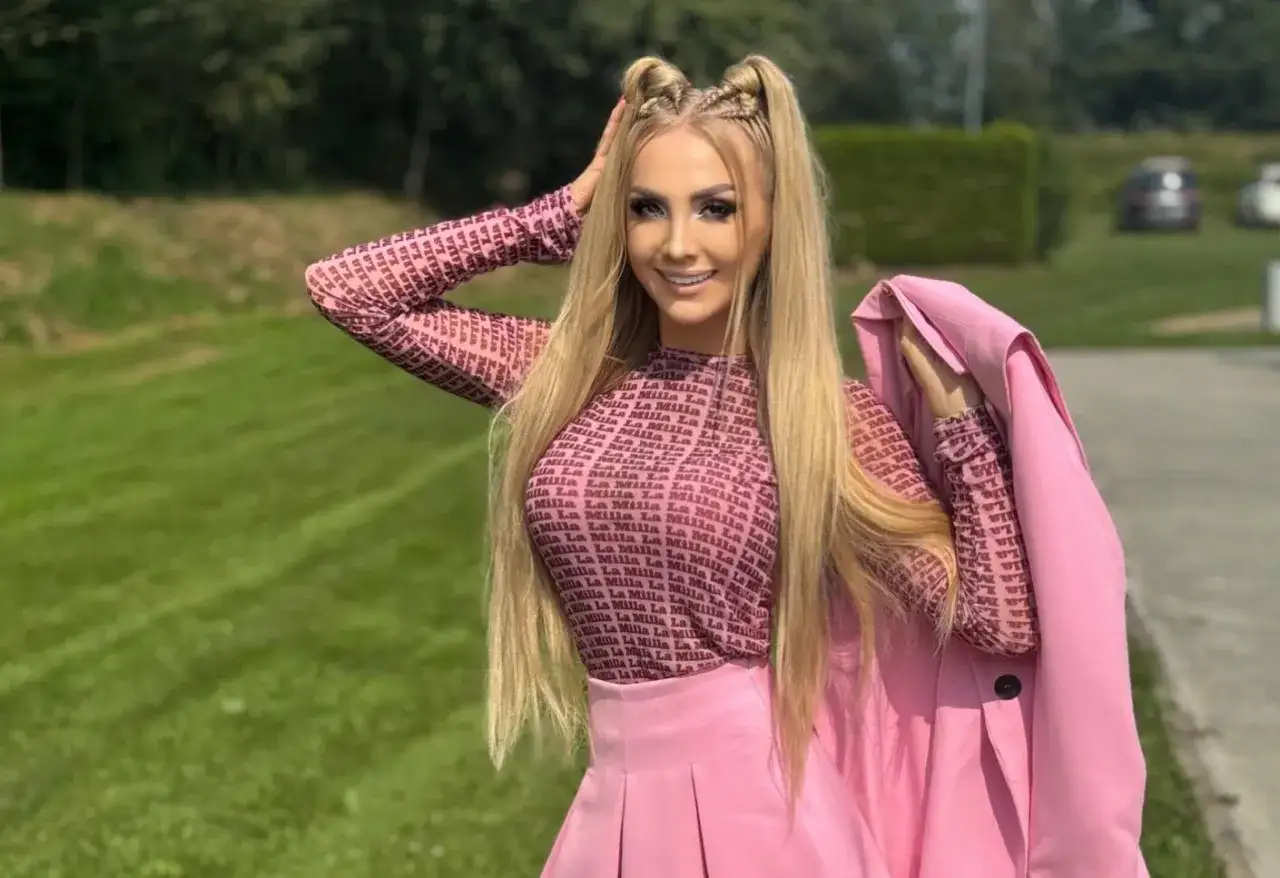 Joanna Narożna w różowej stylizacji, z włosami upiętymi w dwa kucyki, pozuje na tle zielonej trawy.