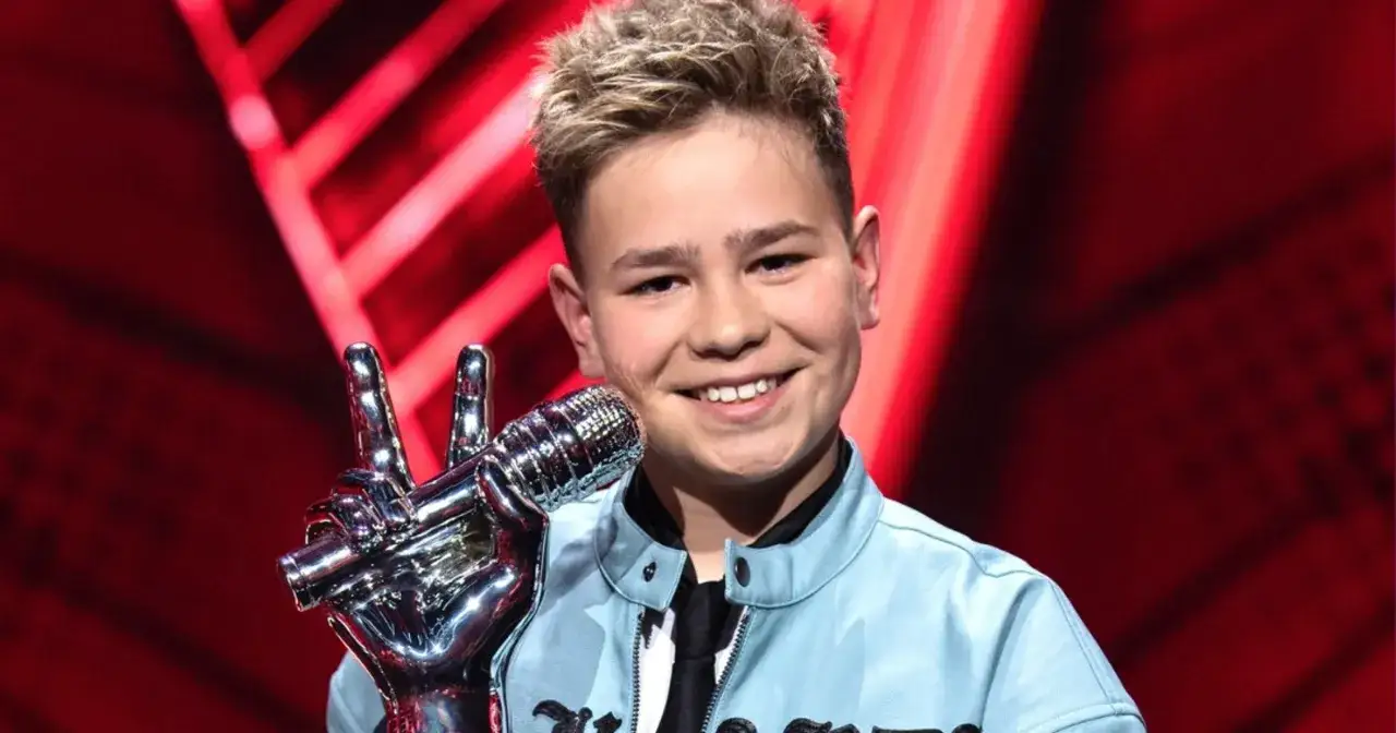 Uśmiechnięty chłopiec z blond włosami trzyma mikrofon w kształcie dłoni. To on wygrał The Voice Kids!